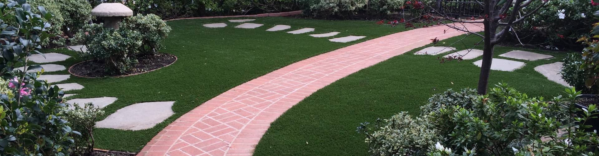 Southwest Greens lawn turf grass alongside a curved brick pathway with stepping stones, garden statue, and lush flowering shrubs.